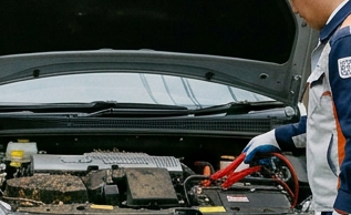 Two roadside workers assist beside a disabled Toyota with its hood open